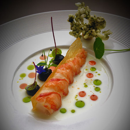 Ein Gourmetgericht mit Hummer, dekoriert mit Kräutern, Essenssoßen und essbaren Blumen.