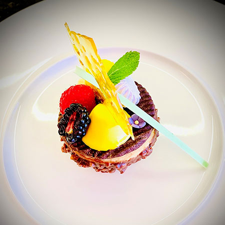 Ein Dessert mit Beeren, Mango, Schokoladenboden und einer Karamell-Dekoration.